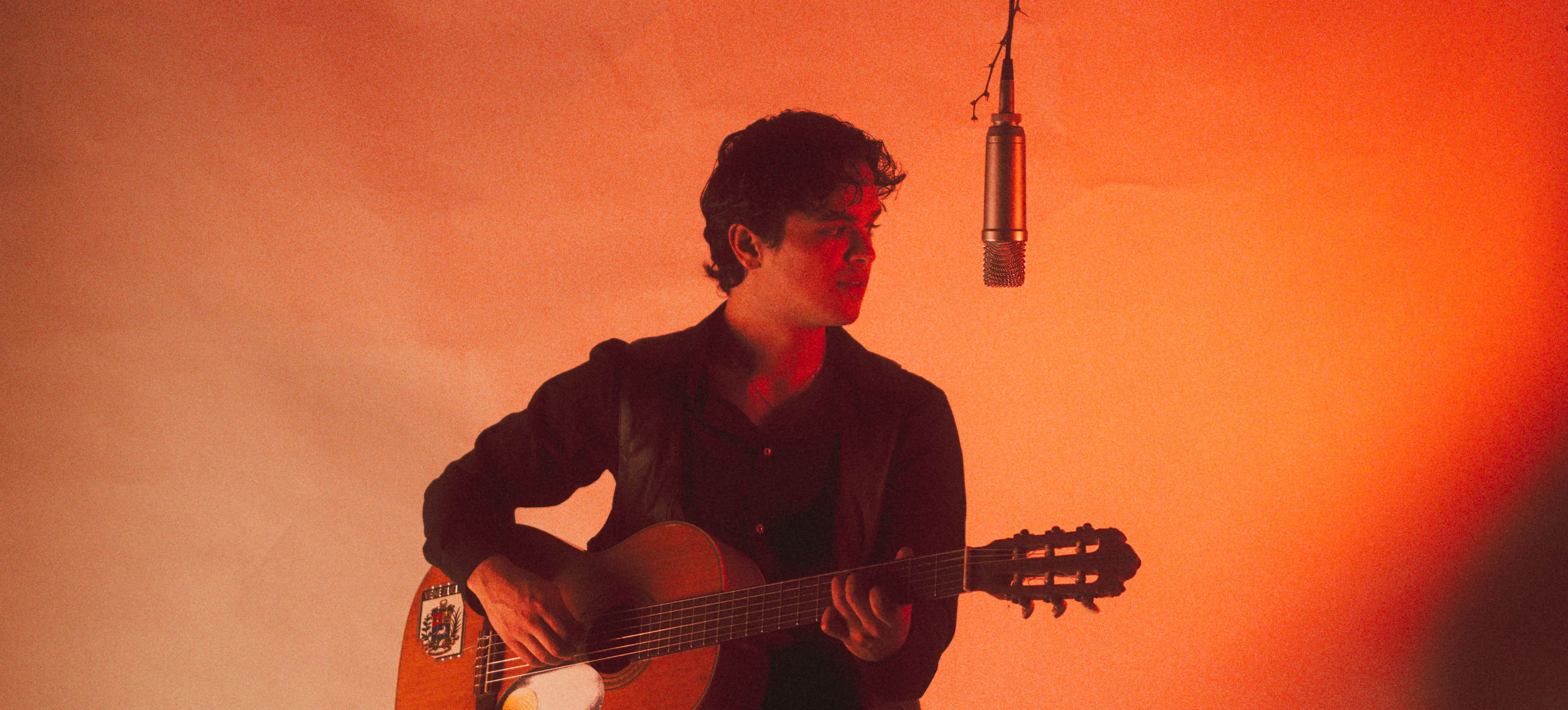 Julio Ávila con su guitarra frente a un micrófono suspendido